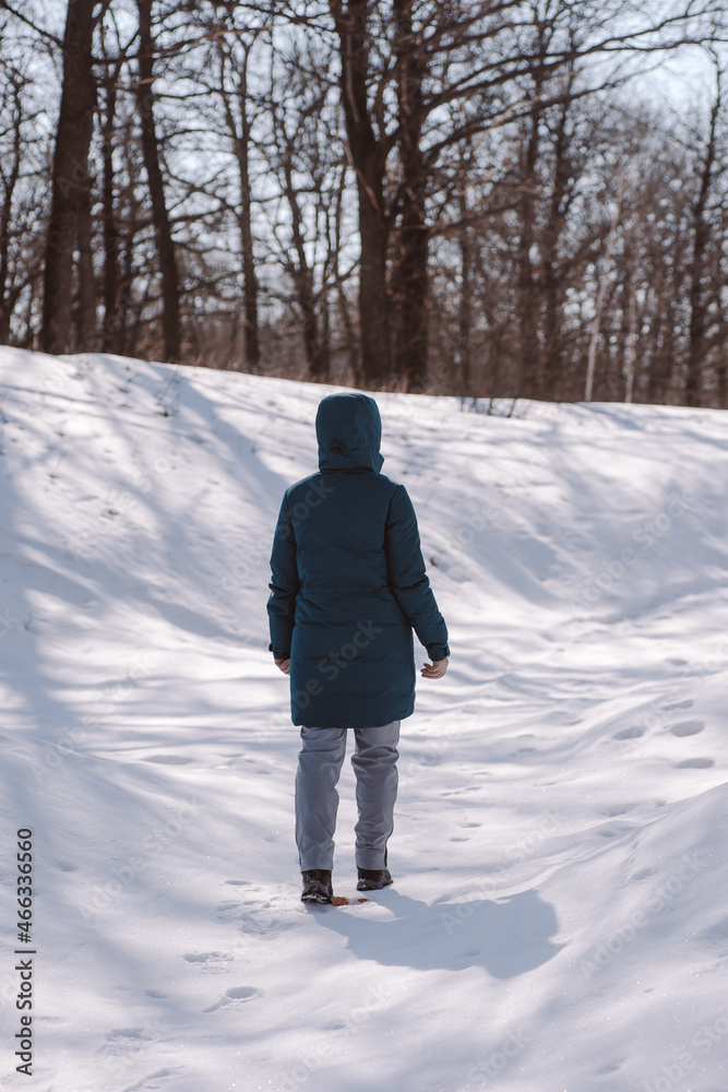 Obraz premium Young woman walks in forest. Caucasian woman stand on road among trees in snowy forest and enjoy sun, rear view.