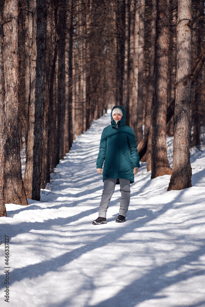 Caucasian woman in snowy forest. Young attractive woman in warm down jacket walk along a rural road covered with snow after blizzard. 
