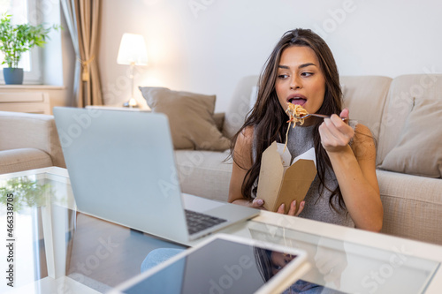 Beautiful woman are eating asian fast food from takeaway box. Delicious Wok noodles. Young woman sitting on the bed and eating her ordered lunch at home. Enjoying at home eating takeaway meal
