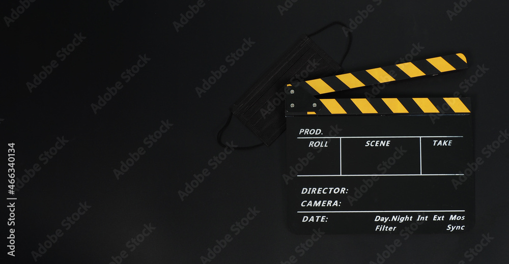 Black with yellow Clapper board or movie slate and black face mask on black blackground.