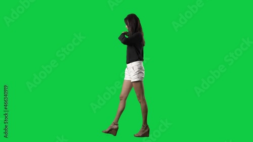 Slow motion side view of walking young slim cocky woman fashion model and tossing hair. Full body isolated on green screen background photo