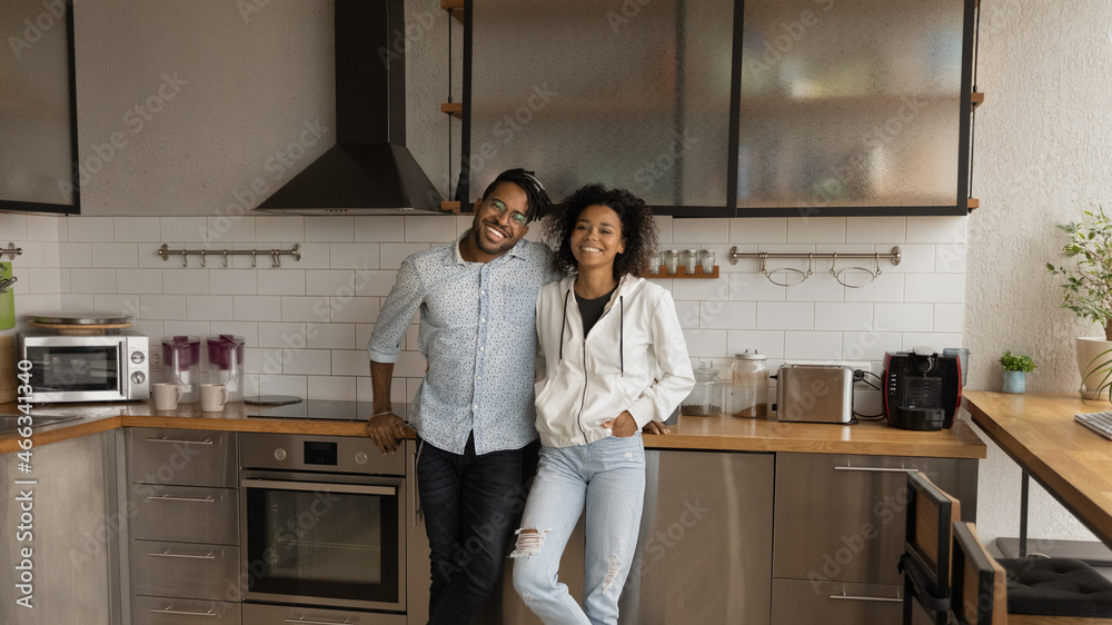 Portrait of happy bonding young mixed race married family couple homeowners posing in modern kitchen, celebrating moving in renovated stylish apartment, real estate dwelling ownership concept. Portrait of happy bonding young mixed race married family couple homeowners posing in modern kitchen, celebrating moving in renovated stylish apartment, real estate dwelling ownership concept.