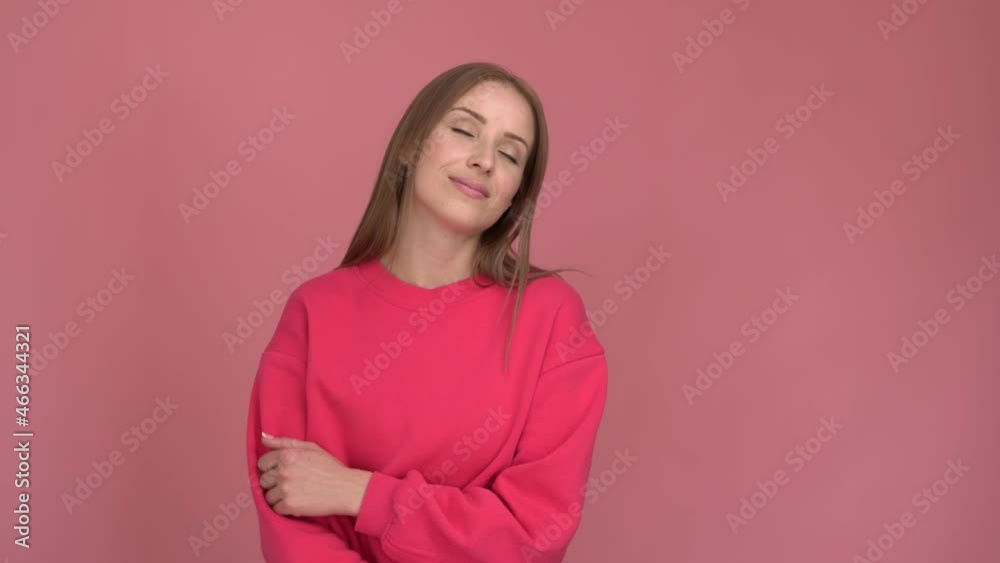 Beautiful caucasian girl straight in front of the camera and listening music with closed eyes. Young woman posing on a pink wall background