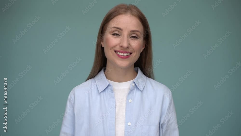 Attractive caucasian girl looking straight into the camera and telling something. Young woman posing on a blue wall background Attractive caucasian girl looking straight into the camera and telling something. Young woman posing on a blue wall background