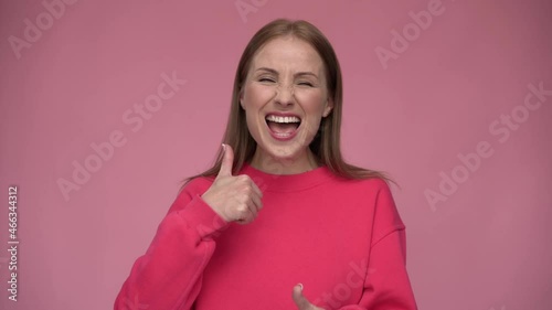 Like. Portrait of optimistic woman showing thumbs up gesture and smiling, meaning well done, good job. Indoor studio shot isolated on pink background