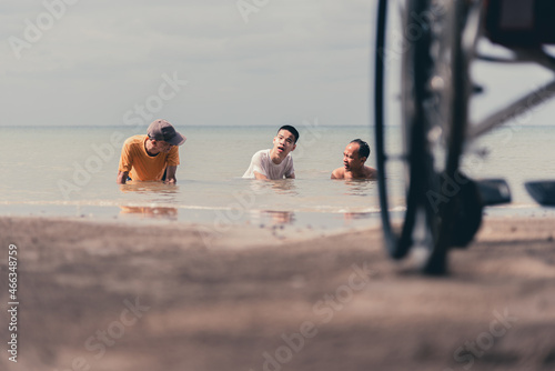 Three men crawl on the sea beach and wheelchair park front of them.