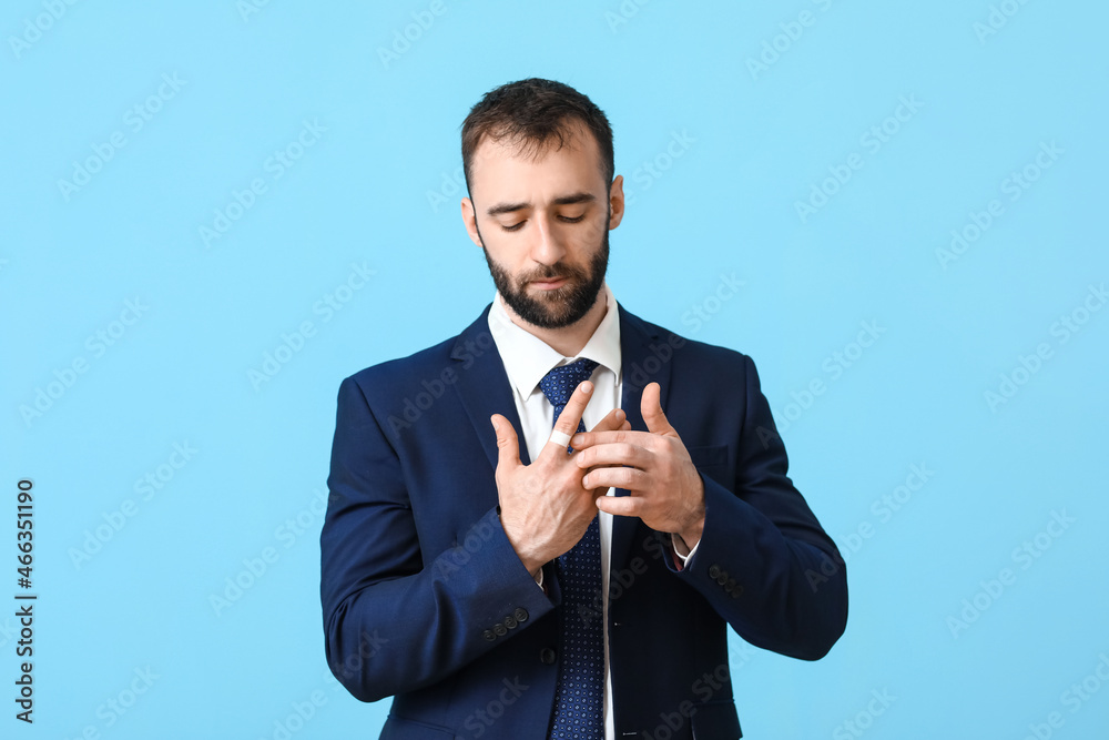 Handsome businessman with plaster onto his finger on blue background Handsome businessman with plaster onto his finger on blue background