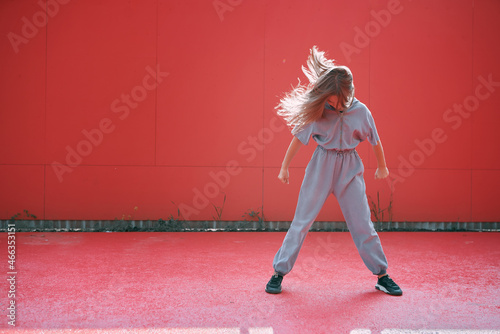 Stylish active teen girl with long waving hairs wearing modern clothes on red background with copy space for advertising