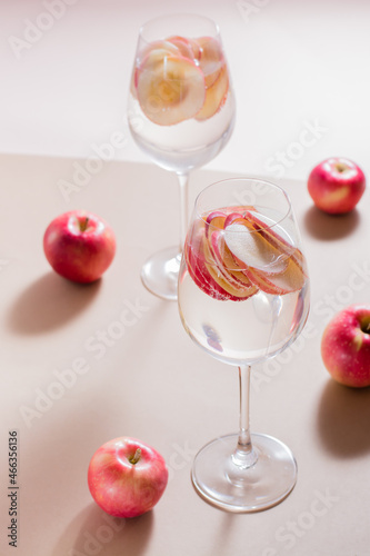 Refreshing cocktail of apple pieces and mineral water in glasses on a brown background in harsh light. Detox wellbeing drink. Vertical view
