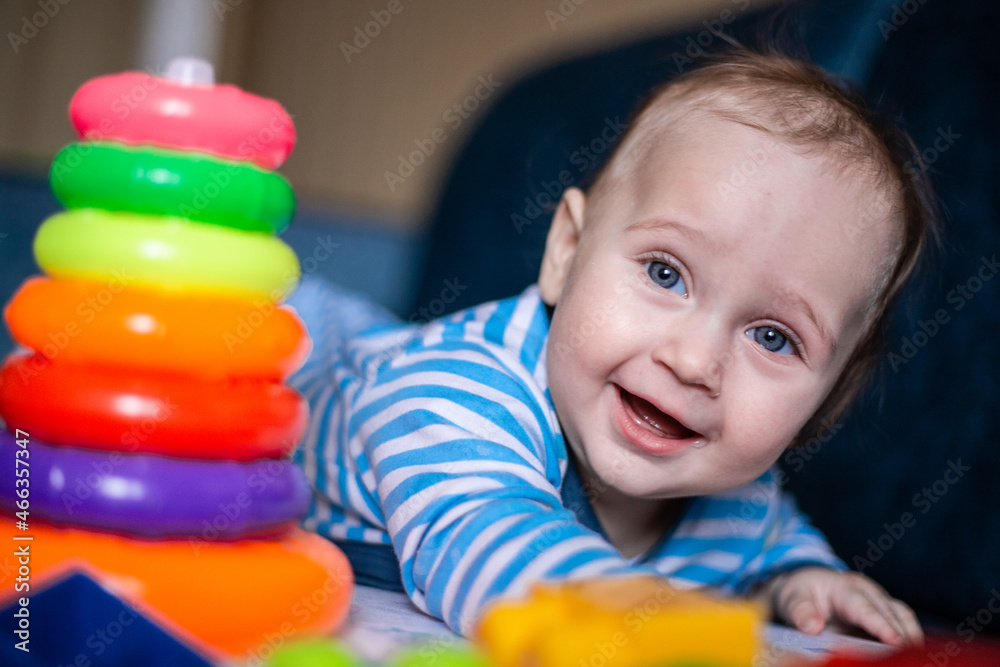 A little kid in a striped suit is lying on his tummy, next to him a children's pyramid and toys. High quality photo A little kid in a striped suit is lying on his tummy, next to him a children's pyramid and toys. High quality photo