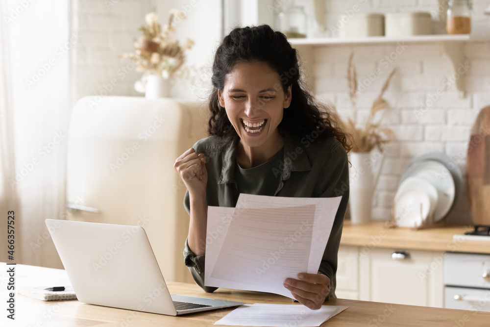 Young excited Hispanic lady sit at table with laptop in domestic kitchen holds papers reading bank notice with good news, learn bank statement, loan repayment, business growth, career advance concept Young excited Hispanic lady sit at table with laptop in domestic kitchen holds papers reading bank notice with good news, learn bank statement, loan repayment, business growth, career advance concept