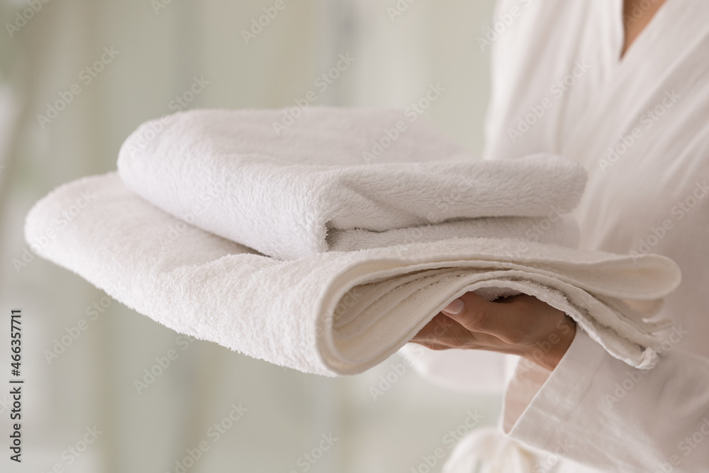 Unrecognizable female wear bathrobe holds carry in hands stack of fresh white fluffy bath towels, close up cropped view. Take a shower, personal hygiene, cleaning service, laundry detergent ad concept