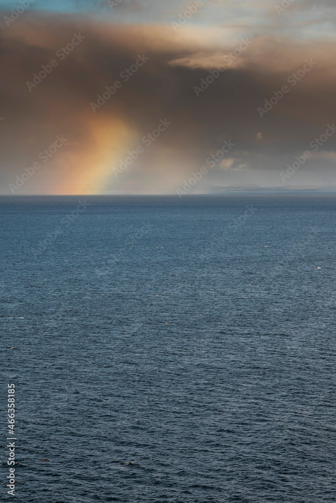 Colorful rainbow symbol of luck over rich blue water surface. Dark dramatic sky. Copy space. Nature wonder. Nobody