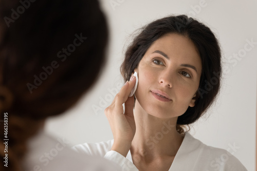 Close up young woman look in mirror holds cotton disc cleanse facial skin, using tonic, micellar water for sensitive dry skin, do evening routine caring about face health and beauty, skincare concept