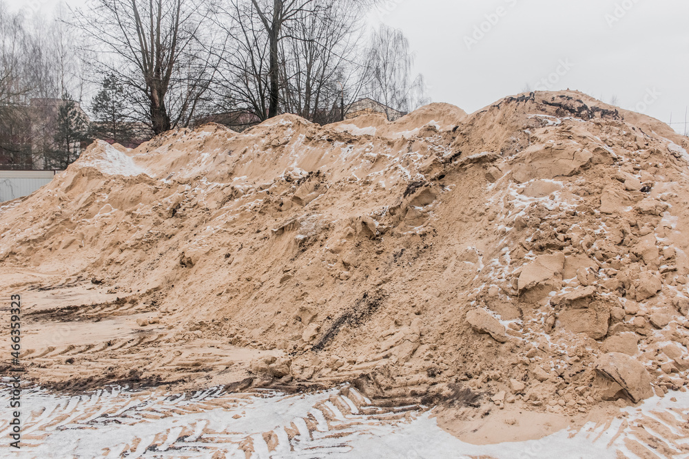 A large pile of sand of natural industrial material is stored outdoors on the territory of the plant