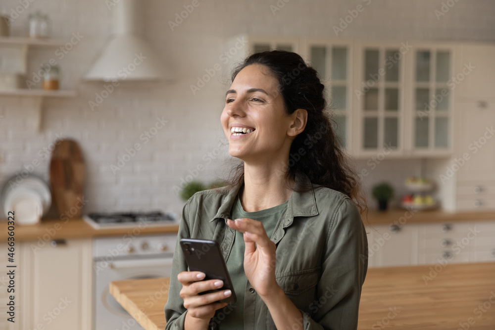 Happy woman standing in kitchen at home with smartphone, smiling enjoy social media chat, e-commerce client buy goods on internet. Modern tech for fun, easy remote e-services for comfort life concept Happy woman standing in kitchen at home with smartphone, smiling enjoy social media chat, e-commerce client buy goods on internet. Modern tech for fun, easy remote e-services for comfort life concept