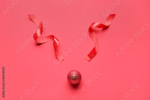 Creative composition with reindeer face made of Christmas ball and ribbons on red background