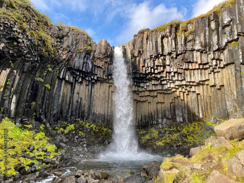 Color vertical photo of Svartifoss waterfall in Iceland. Blue sky with wispy clouds  basalt columns with orange highlights.