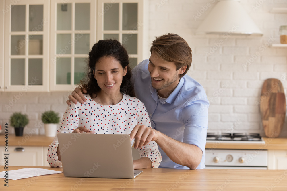 Obraz premium Attractive young couple look at laptop discuss purchase, choose e-services, buy goods, make food order on-line. Satisfied clients of electronic commerce services, modern tech for comfort life concept