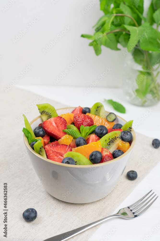 Fresh, healthy chopped fruit salad in a bowl on white  background. Top view. Strawberry, blueberry, kiwi, orange, mint..