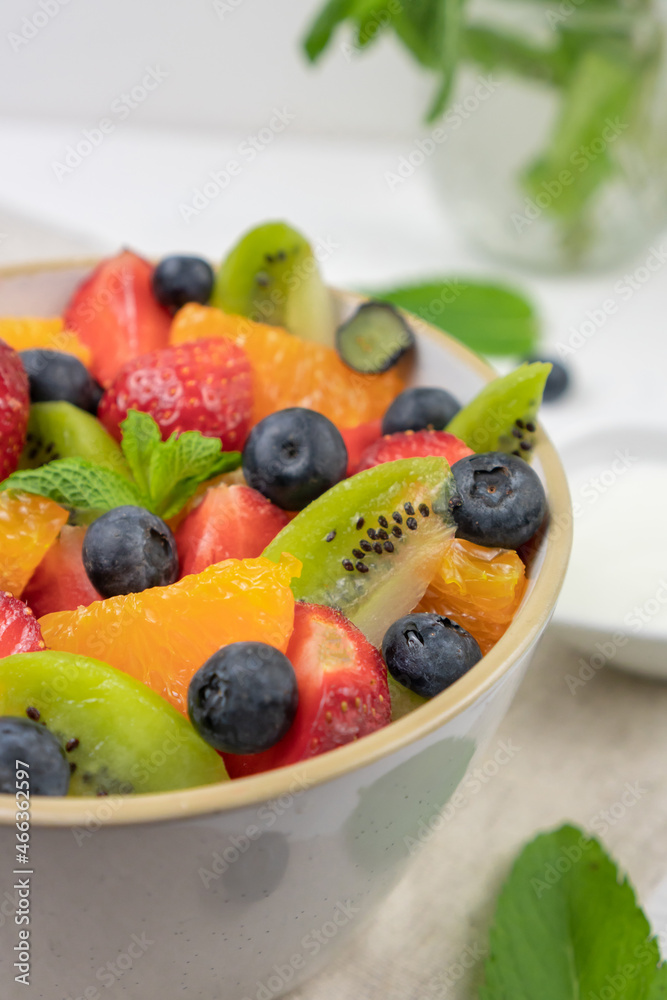 Fresh, healthy chopped fruit salad in a bowl on white  background. Top view. Strawberry, blueberry, kiwi, orange, mint.