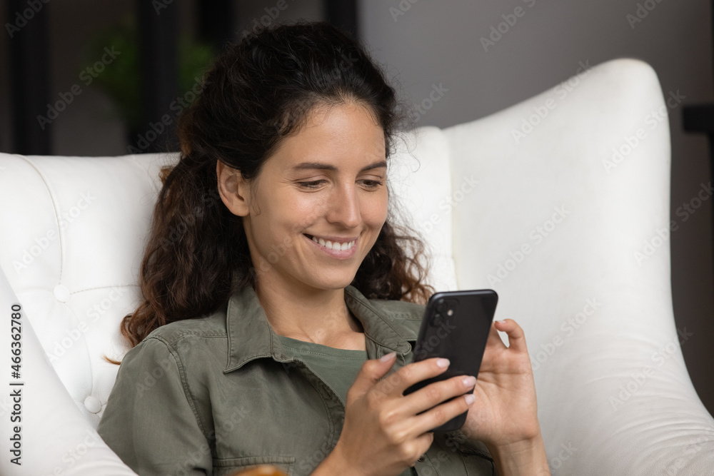 Close up smiling cute Hispanic woman relax on leather cozy armchair with smartphone, enjoy chat in social media, communicates with friend use messenger, spend leisure on internet, modern tech concept Close up smiling cute Hispanic woman relax on leather cozy armchair with smartphone, enjoy chat in social media, communicates with friend use messenger, spend leisure on internet, modern tech concept