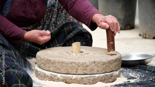 The old woman is grinding flour in the stone mill with the old traditional method. Millstones for grinding wheat into flour, mill traditional production.
