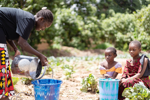 Bild auf Leinwand A tough young black African girl fills a water bucket with water from a metal wa