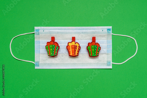 A medical mask on green background with chips - toys in the form of a gift. Top view with copy space, space for text. Celebrating the New Year. Happy New Year 2022 concept.