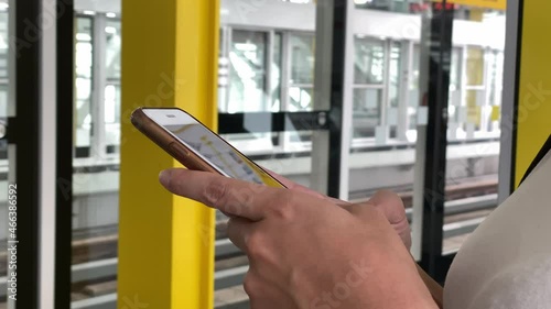 Asian woman stand up on subway plataform using smartphone for check her social network to chat and contact people. Looking phone device while waits the train arrive to station-Dan photo