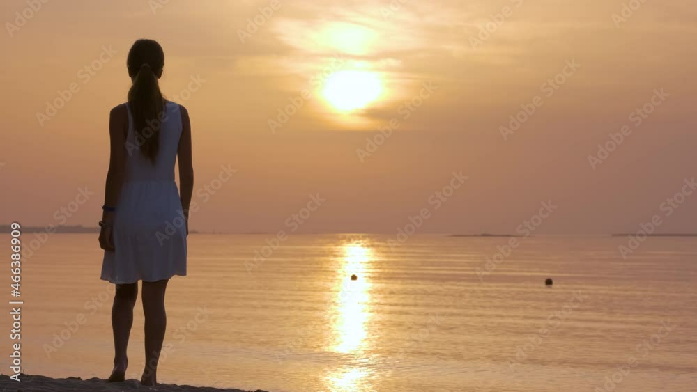 Lonely young woman standing on ocean beach by seaside enjoying warm tropical evening Lonely young woman standing on ocean beach by seaside enjoying warm tropical evening