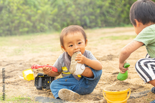 砂場で遊びながら、自分の履いている靴に噛みつく男の子 汚れた靴を口に入れる