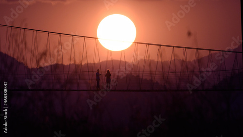 silhouette couple travel on suspention bridge in the twiligt time. photo