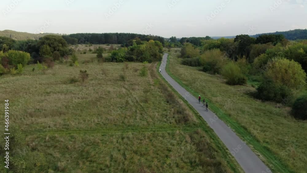 Three youngsters ride bicycle on beautiful flatlands of Lithuania, aerial following view