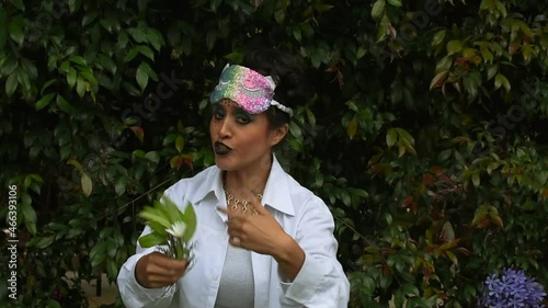Latin woman in disguise with a make-up face and a colorful mask on her forehead talking and making movements with her arms and facial expressions in a nature background