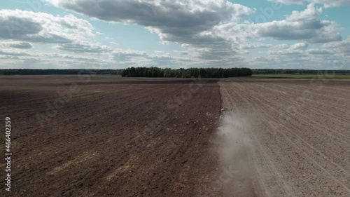 AERIAL VIEW, FROM BEHIND: flock of hungry birds flying behind a tractor with a plow cultivating the soil on arable land. An agricultural machine on picturesque farmland against a cloudy sky. Concept photo