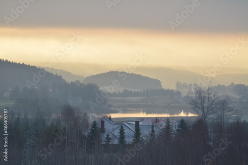 Zimowy wschód słońca nad jeziorem i lasami z mgłą