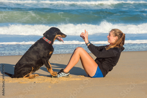 beautiful young woman doing a sit-up session on the beach with the help of her dog photo