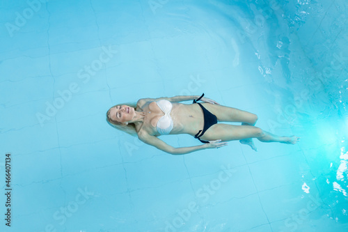 Attractive young woman floating in a swimming pool with her arms outstretched  looking at the sky