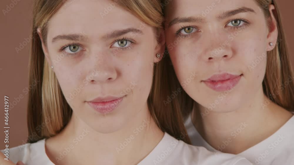 Extreme close up portrait with PAN of pretty young twin sisters looking at camera while posing isolated against brown background Extreme close up portrait with PAN of pretty young twin sisters looking at camera while posing isolated against brown background