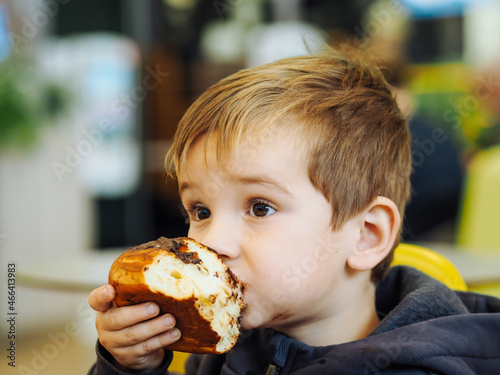 Cute toddler boy in  casual clothes eating a chocolate bun in a food court