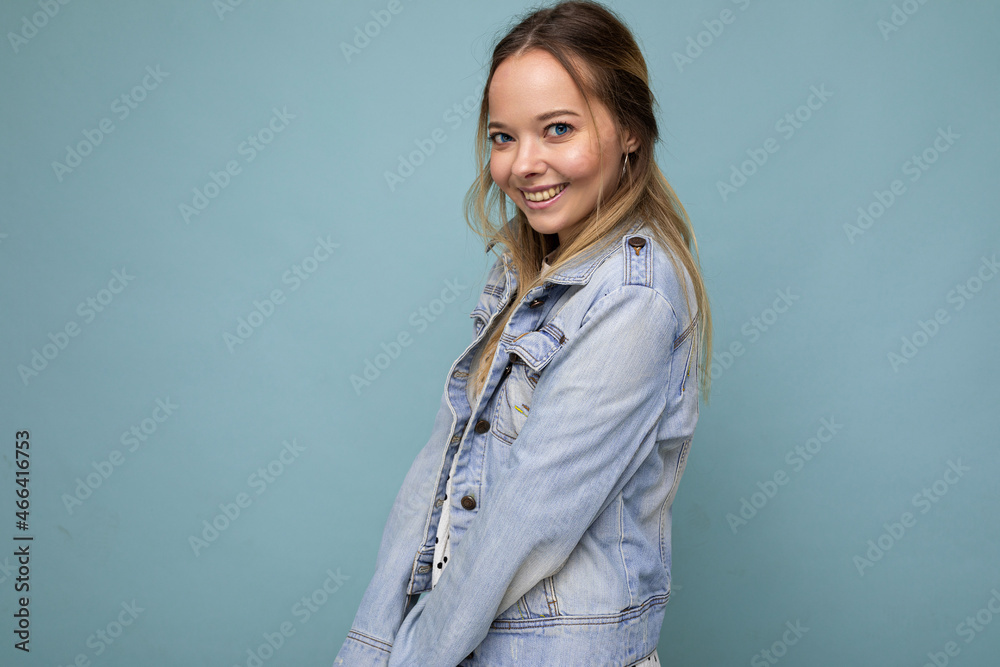 Portrait of young beautiful smiling hipster blonde woman in trendy dress and jean jacket. Sexy carefree female person posing isolated near blue wall in studio. Positive model with natural makeup. Copy Portrait of young beautiful smiling hipster blonde woman in trendy dress and jean jacket. Sexy carefree female person posing isolated near blue wall in studio. Positive model with natural makeup. Copy