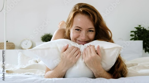 Portrait of happy beautiful young woman with red hair enjoying morning in pajamas on bed in comfortable conditions. girl woke up in  good mood lying on bed laughing and cuddling up to pillow.