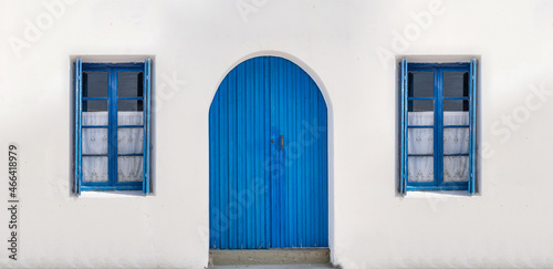 Blue wooden door on whitewashed wall windows with opened shutters and curtains background.