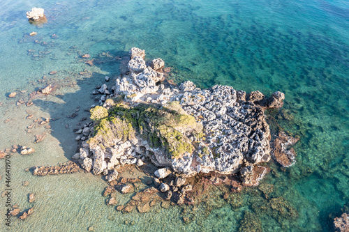 Aerial drone view of rocky formation with moss on it in blue Aegean sea.