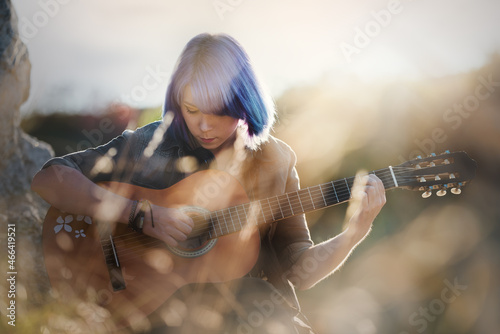 Woman with purple-blue hair playing guitar in sunny nature.