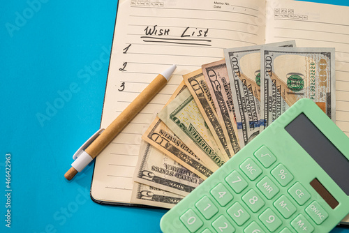 notebook with a wish list on the side of dollars and a pen lie on a blue background