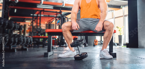 Close up of athletic man is sitting on a sports bench. The dumbbell lies near the athlete's feet. Sport banner