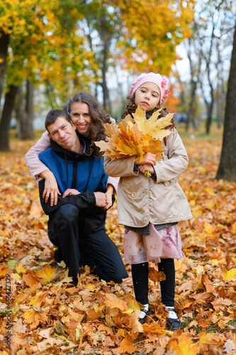 Portrait of a family in an autumn park. Happy parents and unhappy child posing with yellow leaves.