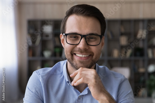 Head shot portrait of smiling joyful intelligent young businessman in eyeglasses. Happy confident millennial employee entrepreneur looking at camera, holding video call meeting, virtual event concept.